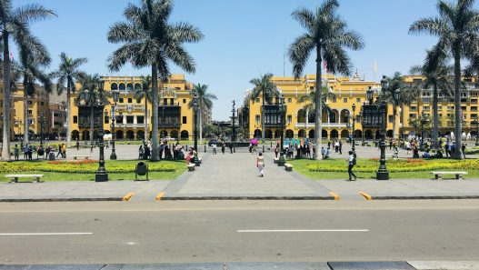 Plaza de Armas in Lima, Peru, with palm trees and people walking on a sunny day