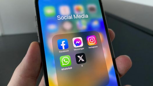 Hand holding a phone with social media apps including X, how to retweet