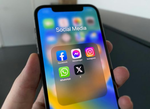 Hand holding a phone with social media apps including X, how to retweet